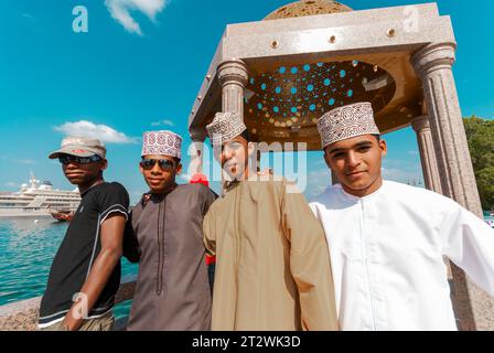 Felici giovani uomini locali in abiti tradizionali e occidentali sorridono per la macchina fotografica a Mutrah Muscat in Oman Foto Stock
