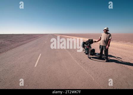 Un turista solitario in bicicletta fa una pausa sulla strada principale del deserto a sud dell'Oman Foto Stock