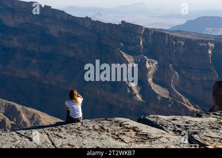 Una donna bionda è seduta ai margini di Jebel Shams e gode della vista della valle sottostante in Oman Foto Stock