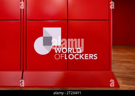 Cartello con il logo World of Lockers sull'esterno di un armadietto rosso. L'azienda offre tecnologia per la logistica. I client possono ricevere facilmente i pacchetti. Foto Stock