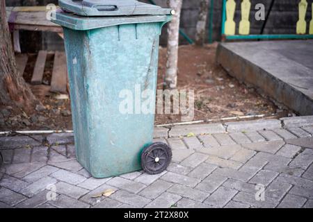 I bidoni della spazzatura verde sono sul lato della strada. Sembra logoro con il colore che inizia a sbiadirsi. Foto Stock