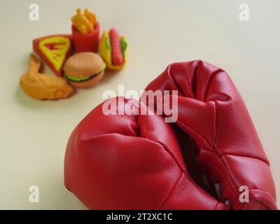 Immagine ravvicinata di guanto da boxe e cibi spazzatura come hamburger e patatine fritte. Combattere le cattive abitudini alimentari. Foto Stock