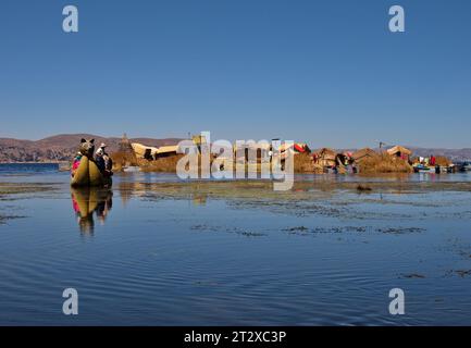 Uomo Uros che trasporta turisti su una barca a canne vicino alla sua isola galleggiante sul lago Titicaca Foto Stock