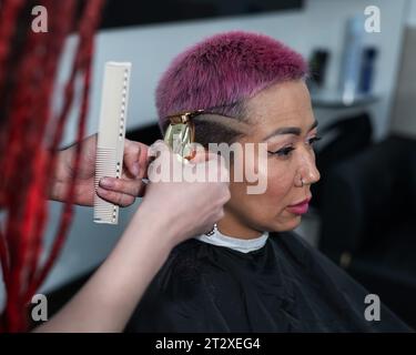 Il parrucchiere rasa il tempio di una cliente femminile. Donna asiatica con capelli corti rosa in barbiere. Foto Stock