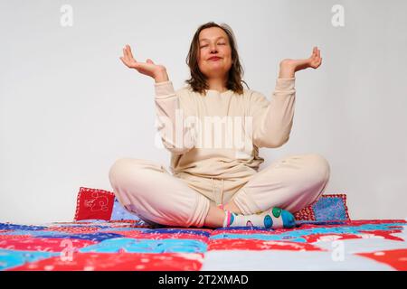 Donna che medita in posa di loto seduta sul tappeto a casa Foto Stock