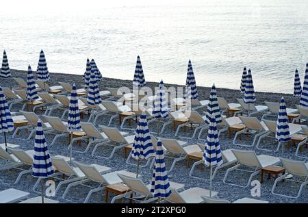 Ombrelloni blu e bianchi a righe e lettini sulla spiaggia della città. Ombrelloni sulla spiaggia sullo sfondo del mare Foto Stock