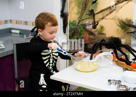 Ragazzo vestito come uno scheletro che prepara i biscotti di halloween. Felice ragazzo che si prepara per halloween. Festival in cucina. Foto Stock