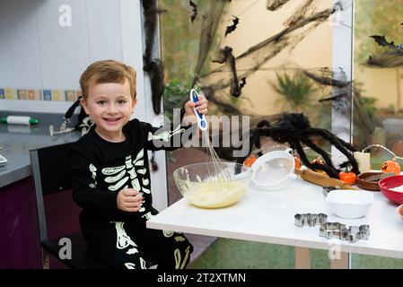 Ragazzo vestito come uno scheletro che prepara i biscotti di halloween. Felice ragazzo che si prepara per halloween. Festival in cucina. Foto Stock