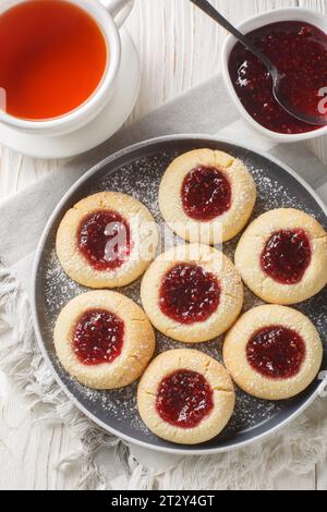I biscotti con impronte digitali sono dei classici biscotti a base di zucchero con un primo piano centrale ripieno di marmellate sul piatto sul tavolo di legno bianco. Vista dall'alto verticale Foto Stock