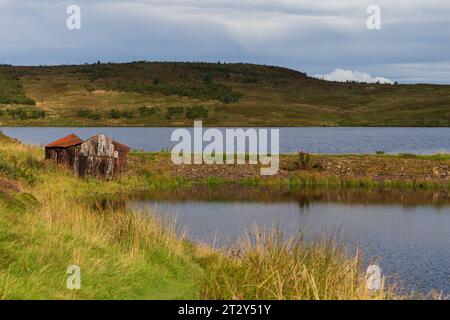 Una rovina di una baracca ai margini di un lago in Scozia in una soleggiata mattinata estiva durante una mattinata estiva Foto Stock