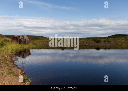 Una rovina di una baracca ai margini di un lago in Scozia in una soleggiata mattinata estiva durante una mattinata estiva Foto Stock