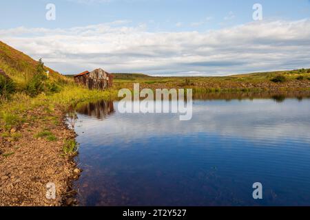 Una rovina di una baracca ai margini di un lago in Scozia in una soleggiata mattinata estiva durante una mattinata estiva Foto Stock