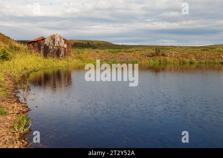 Una rovina di una baracca ai margini di un lago in Scozia in una soleggiata mattinata estiva durante una mattinata estiva Foto Stock