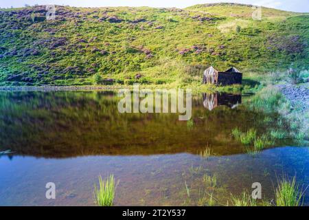 Una rovina di una baracca ai margini di un lago in Scozia in una soleggiata mattinata estiva durante una mattinata estiva Foto Stock
