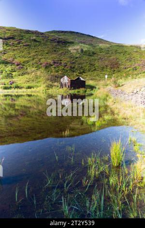 Una rovina di una baracca ai margini di un lago in Scozia in una soleggiata mattinata estiva durante una mattinata estiva Foto Stock