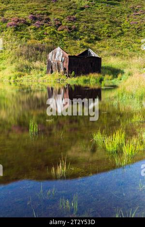 Una rovina di una baracca ai margini di un lago in Scozia in una soleggiata mattinata estiva durante una mattinata estiva Foto Stock