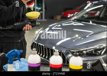 Il master applica una composizione speciale al dispositivo per la lucidatura della superficie della carrozzeria della vettura. Foto Stock