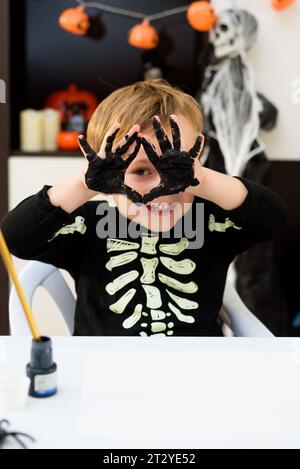 Un bambino vestito come uno scheletro mostra oggetti di ragno e fantasmi. Festa di Halloween Foto Stock