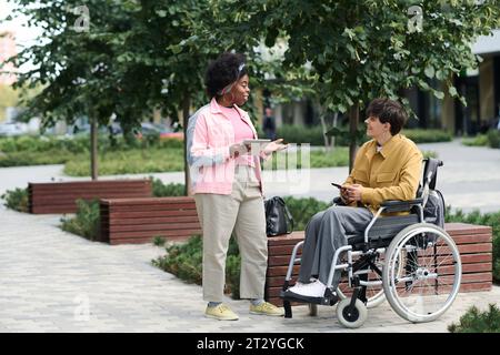 Coppie multietniche che utilizzano gadget mentre trascorrono il tempo all'aperto Foto Stock