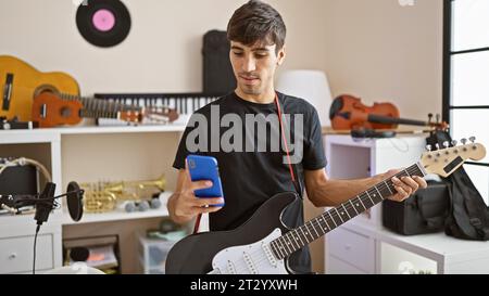 Giovane chitarrista maschile ispanico, che compone le melodie elettroniche, invia SMS mentre affronta la chitarra elettrica nello studio musicale Foto Stock