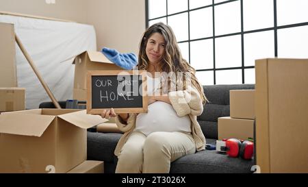 Giovane donna incinta che tiene una lavagna che tocca la pancia nella nuova casa Foto Stock