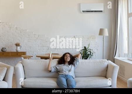 Una donna allegra e rilassata che possiede il telecomando dell'aria condizionata Foto Stock
