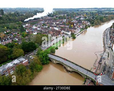 Bewdley, Worcestershire, 22 ottobre 2023. Le barriere alluvionali sono state dispiegate mentre il fiume Severn continua a salire dopo Storm Babet, con i livelli previsti per il picco lunedì sera. L'attuale lavoro per l'installazione di barriere di inondazione aggiuntive è stato ostacolato dall'aumento del livello dell'acqua. Un treno a vapore parte dalla stazione ferroviaria di Severn Valley G.P. Essex/Alamy Live News Foto Stock