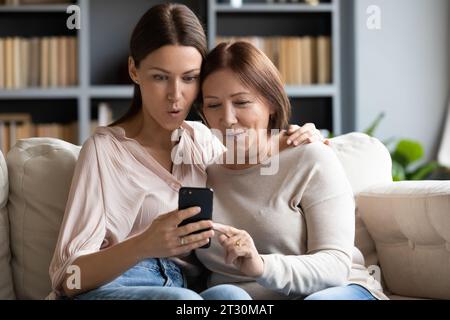 La figlia adulta anziana madre che sta leggendo le notizie tramite smartphone si sente stupita Foto Stock