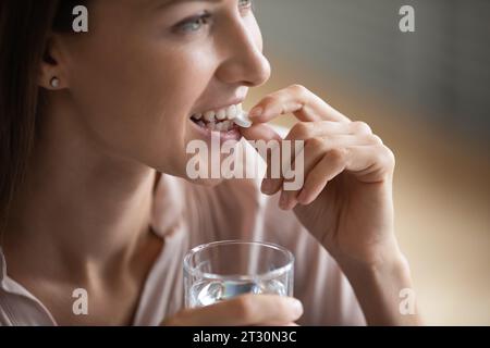 Closeup donna in possesso di un bicchiere d'acqua che assume vitamine a dose giornaliera Foto Stock