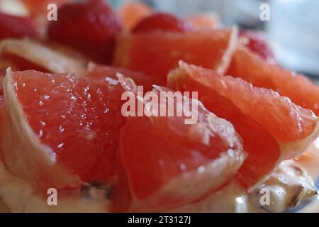 Pezzetti di pompelmo sbucciati sopra lo yogurt. Lamponi sfocati sullo sfondo. Fa parte di una deliziosa colazione. Foto Stock