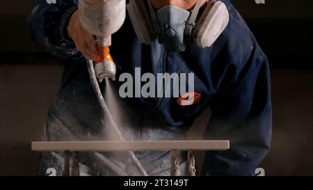 Primo piano di un falegname maschio che spruzza vernice o primer con aria compressa su un pannello di legno. Creativo. Produzione di mobili. Foto Stock
