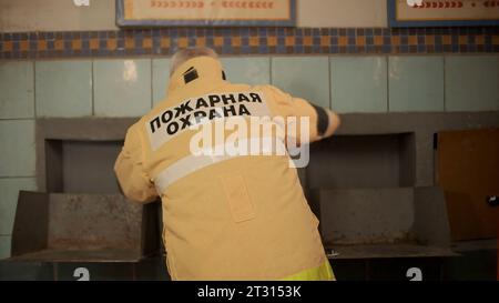 Vista posteriore di un vigile del fuoco che si prepara per la chiamata. Clip. Uomo che si veste di giacca protettiva. Foto Stock