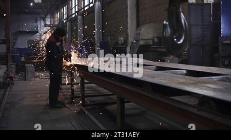 Lavoratore senza casco in fabbrica con saldatura. Clip. Scintille di saldatura volano dal ferro in fabbrica. L'uomo lavora con saldature pericolose senza maschera a. Foto Stock