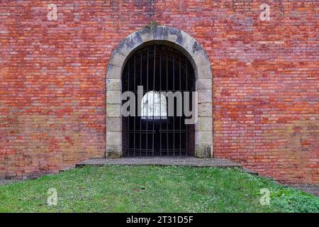 Un passaggio chiuso da un traliccio in un vecchio muro di fortezza in mattoni. Mattoni antichi. Foto Stock
