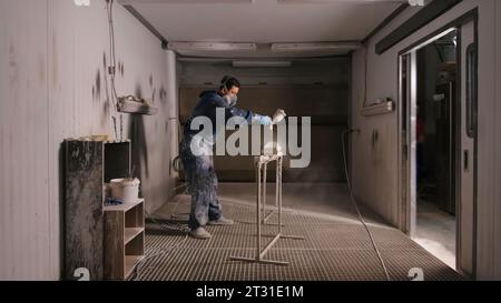 Il lavoratore dipinge pannelli di legno con pistola a spruzzo. Creativo. Il lavoratore dipinge prodotti in legno con pistola a spruzzo in officina. Officina di verniciatura per la pittura del legno Foto Stock