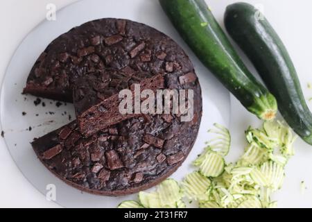 Fetta di torta al cioccolato zucchine sulla torta rotonda. Torta al cioccolato doppia umida con zucchine grattugiate, polvere di cocco, cioccolato e goccia di cioccolato Foto Stock
