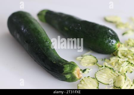 Zucchine lussureggianti e verdi, una specie di zucchine vegetali o altrimenti chiamato midollo infantile fotografate su sfondo bianco insieme a zucchine grattugiate. Foto Stock