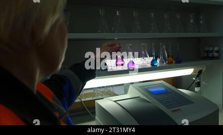 Germania - Berlino, 15 maggio 2023: Una donna in laboratorio versa il liquido nelle fiasche. Clip. La donna in uniforme versa liquido colorato per l'analisi chimica. Donna Foto Stock