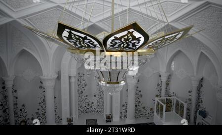 Un lampadario molto costoso in una sala elegante. Scena. Splendidi interni bianchi di una sala concerti o ristorante vuota. Foto Stock