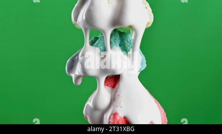 Il cioccolato bianco al rallentatore viene versato sulle meringhe dolci. Clip di scorta. Dessert davanti a fondo cromatico verde. Foto Stock