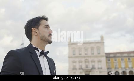 Un bell'uomo in completo cammina lungo la strada il giorno d'estate. Azione. Un uomo attraente in completo va in data o in occasione di un evento. Un uomo elegante in completo cammina con sicurezza Foto Stock