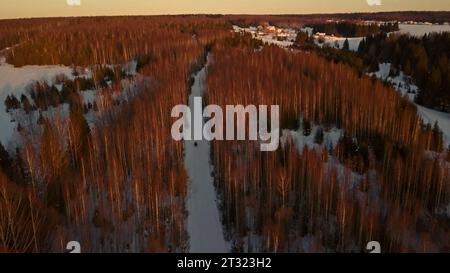 Vista invernale da un elicottero. Clip. Piccoli villaggi nel mezzo di foreste su cui cala la luce del sole. Foto Stock