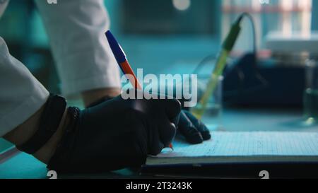 L'assistente di laboratorio scrive i risultati nel notebook. Stock di filmati. Lo scienziato registra i risultati dell'esperimento. Il chimico esegue analisi o esperimenti Foto Stock