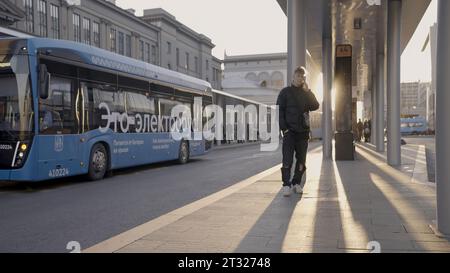 Serbia, Belgrado - 12 aprile 2023: Il giovane parla al telefono alla fermata dell'autobus. Azione. Il giovane aspetta l'autobus alla fermata dell'autobus nelle giornate di sole. Moderno Foto Stock