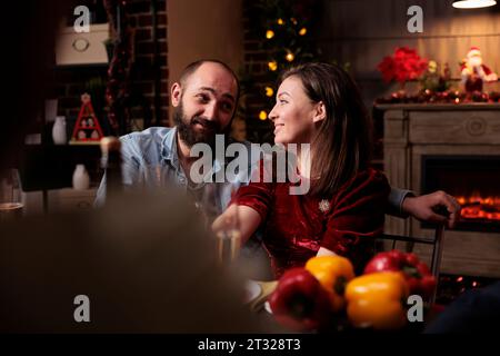 Dolce gente che incontra la famiglia a cena la vigilia di natale, radunandosi intorno a un tavolo con amici e parenti per mangiare cibo tradizionale e bere vino. Coppia che parla con persone durante l'evento di dicembre. Foto Stock