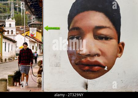 Bogotà, Colombia - 2 gennaio 2023: Il giovane cammina davanti a un murale nel quartiere la Candelaria Foto Stock