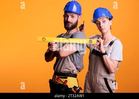 Gli operai edili che tengono il cacciavite e il livello dell'acqua nelle riprese da studio, utilizzando un righello o un livellatore per lavori di ristrutturazione. Team di esperti di costruzione sicuri degli strumenti di ristrutturazione. Foto Stock