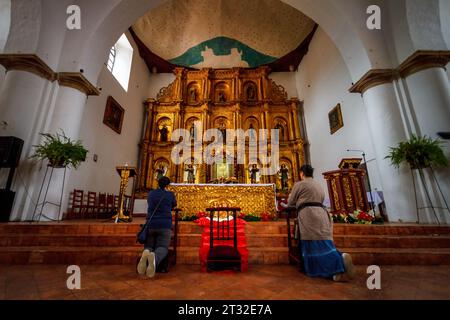 Villa de Leyva, Colombia - 5 gennaio 2023: Due donne pregano davanti all'altare della parrocchia principale della città Foto Stock