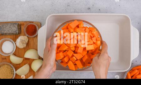 Ricetta per zuppa di zucca arrostita. Cubetti di zucca sbucciati e senza semi, carota, cipolla, aglio e spezie da vicino in una teglia da forno in ceramica inclusa nel kit Foto Stock