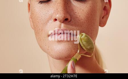 Foto ravvicinata e ritagliata di una giovane che utilizza un rullo sulla pelle lentigginata Foto Stock